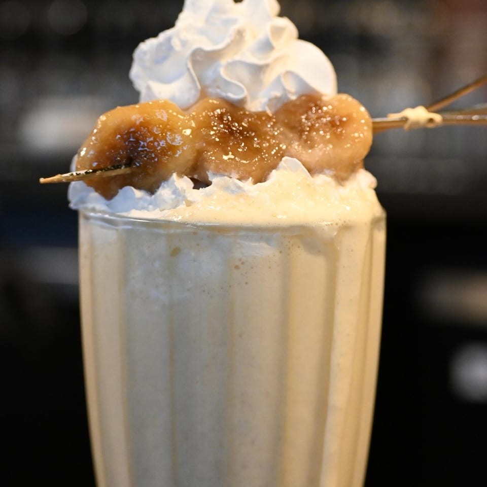Creamy milkshake topped with whipped cream and caramelized banana skewers in a tall glass.