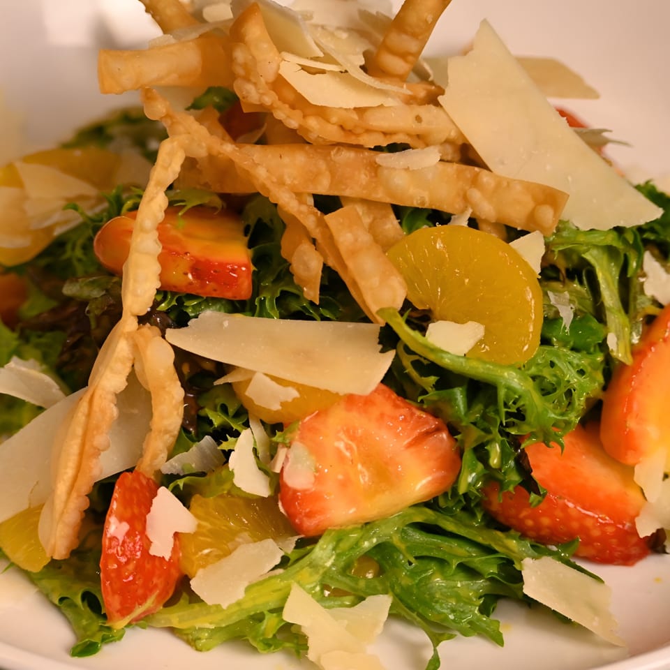 A vibrant salad with green lettuce, strawberries, orange slices, parmesan, and crispy wonton strips.