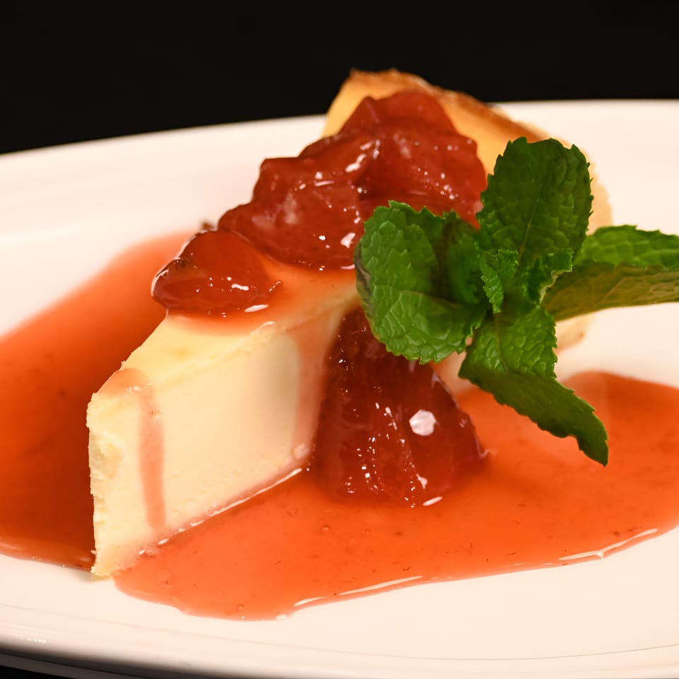 Slice of cheesecake with strawberry topping and mint garnish on a white plate.