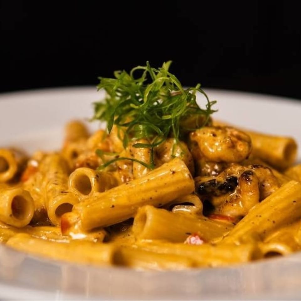 Rigatoni pasta in a creamy orange sauce with shrimp and green garnish on a white plate.