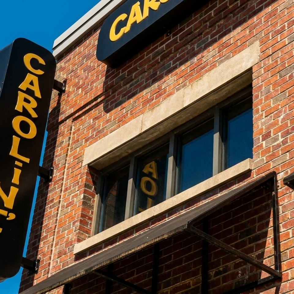 A black vertical sign with yellow letters spelling "CAROLINE'S" hangs on a brick building.