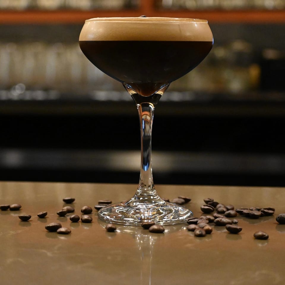 Espresso martini in a coupe glass with coffee beans scattered on a bar top.