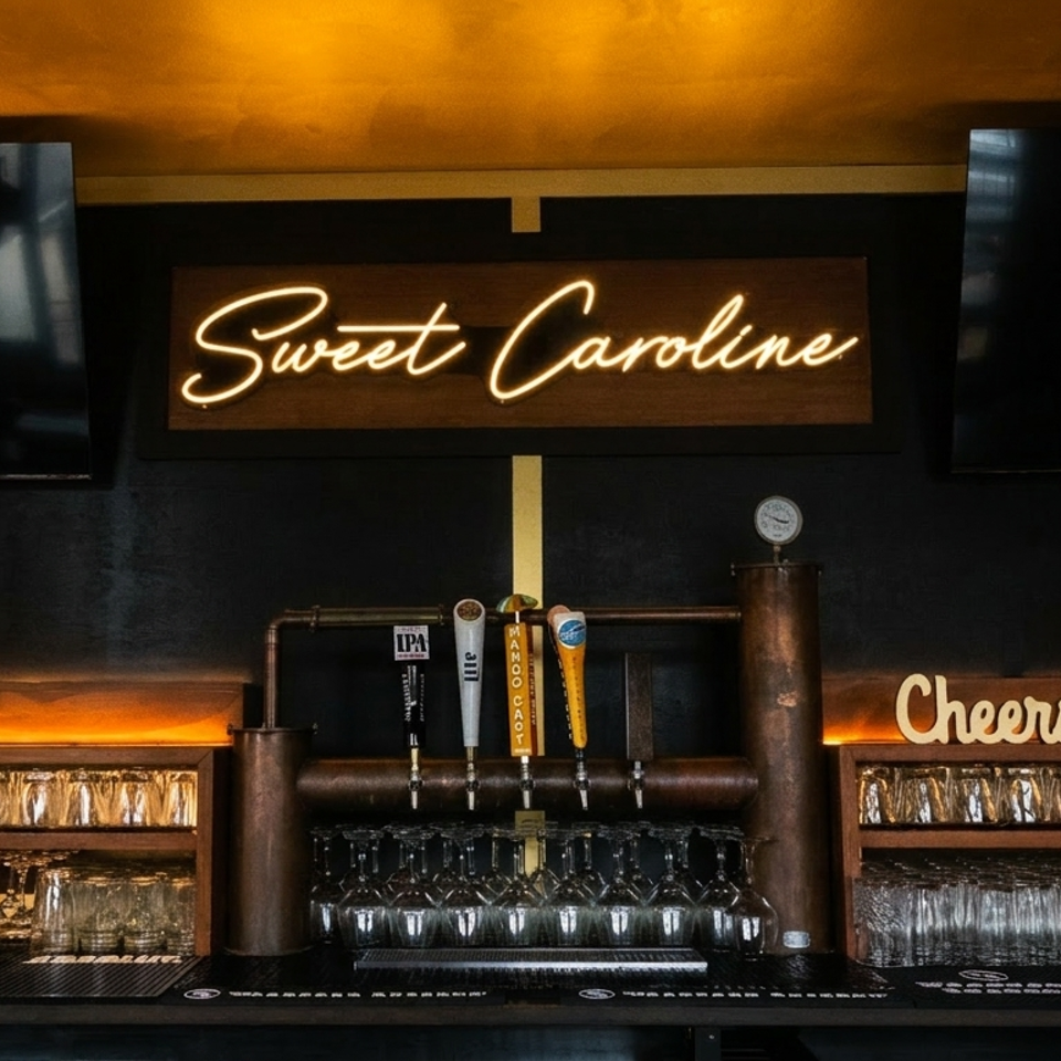 A bar with a "Sweet Caroline" neon sign, beer taps, and shelves of clean glasses.