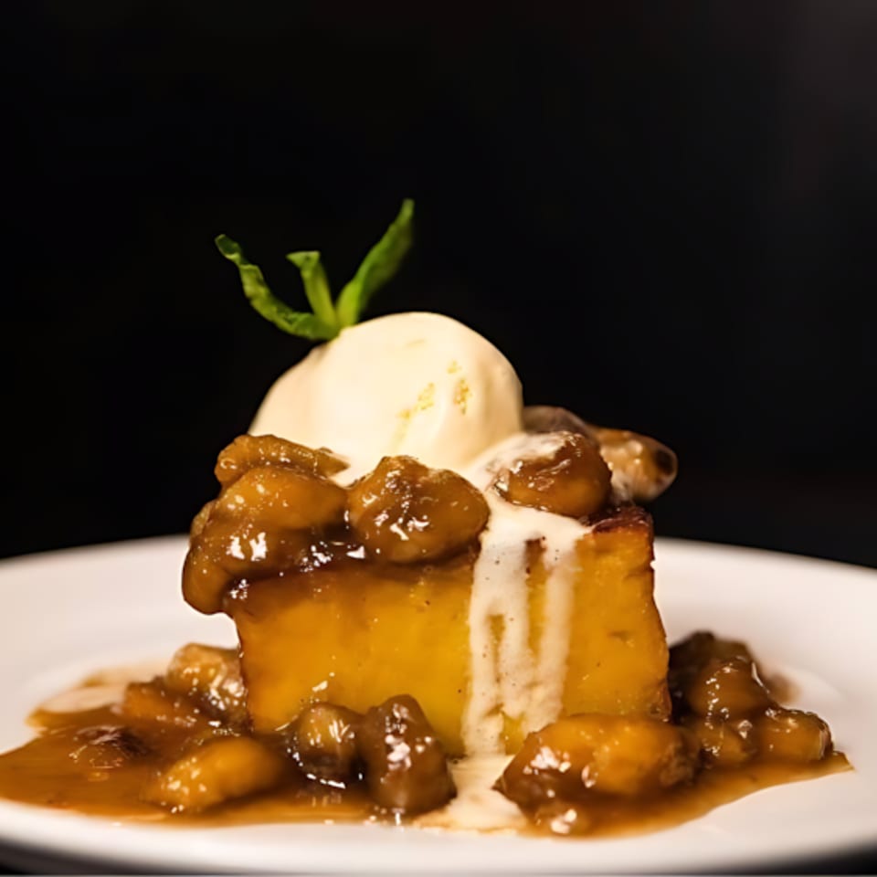 Bread pudding topped with vanilla ice cream, caramelized bananas, and a mint sprig.