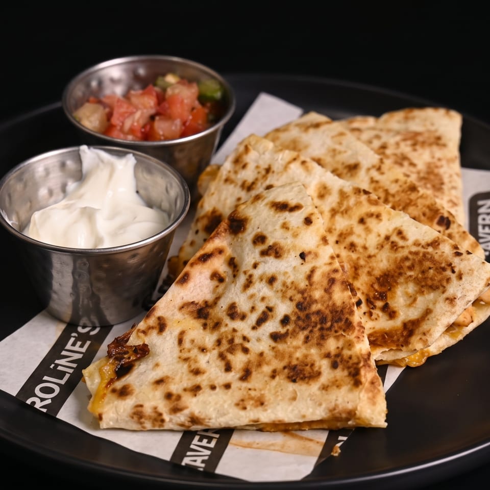 Quesadilla wedges with melted cheese, served with salsa and sour cream on a black plate.
