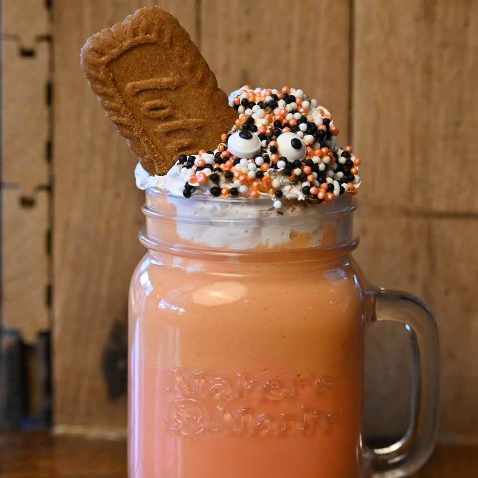 Orange Halloween milkshake in a mason jar, topped with whipped cream, sprinkles, and a cookie.