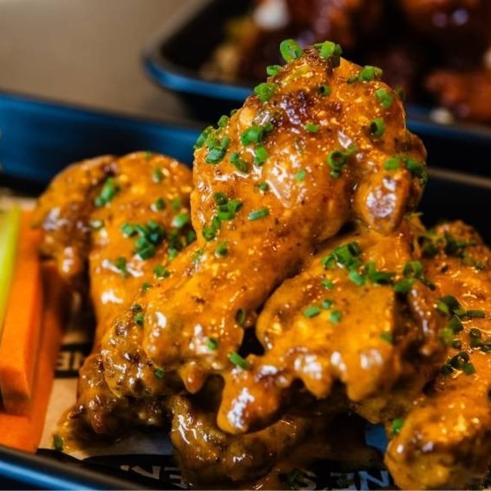 Close-up of golden-brown chicken wings covered in sauce and chives, with celery and carrots.
